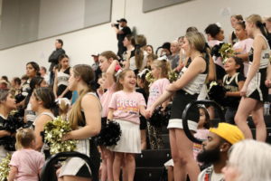 Cheerleader holds hands with a clinic participant at varsity basketball game against Lake Travis.
