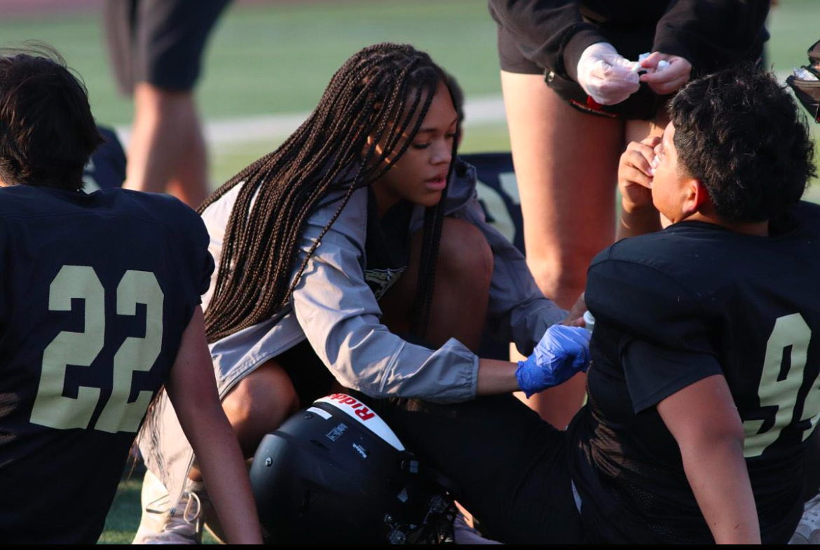 Student Trainer Zaniah Hoskins helping a JV football player with a nosebleed. 