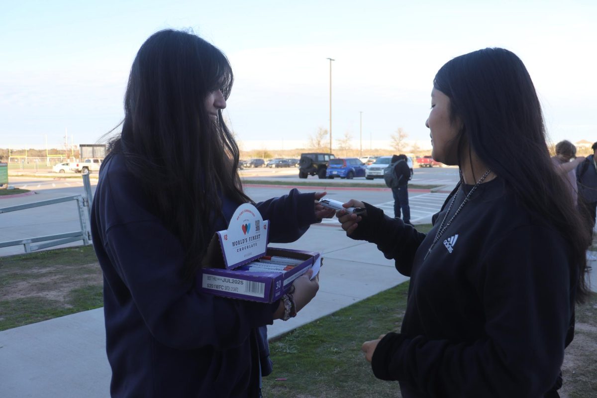 DECA President Mia Garza sells a chocolate bar to a student at the bus pick-up area as part of their chocolate fundraiser.