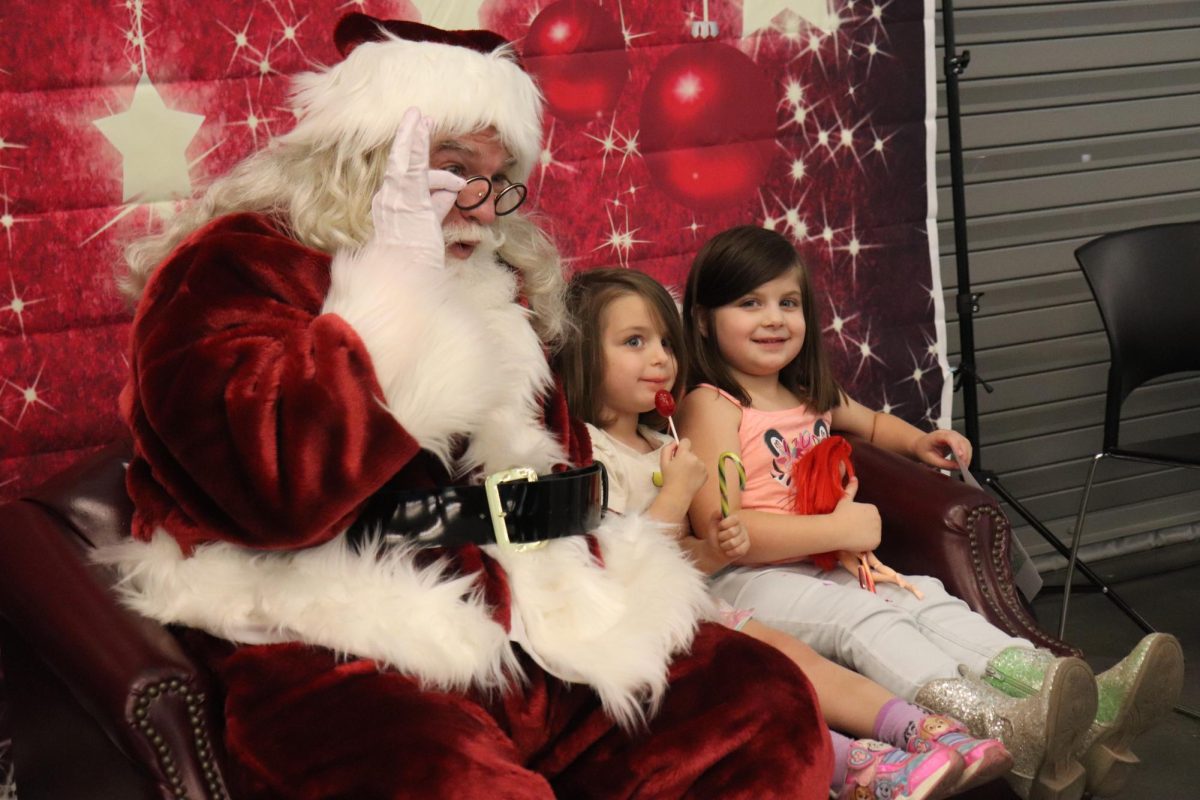 Santa Claus posing with two little girls for a photo after exchanging with him wishes for certain wrapped presents underneath the tree this Christmas.